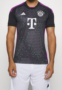 Svart fotbollsjersey med ett gradientmönster av gröna och lila trianglar. Har vitt logotyp och text, korta ärmar och kragdesign.