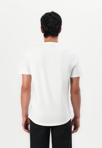 Weißes T-Shirt mit kurzen Ärmeln aus Baumwolle, mit einem runden Ausschnitt und einem leicht gewellten Saum, in einfarbigem Design ohne sichtbare Grafiken.