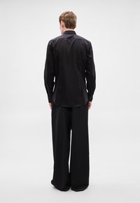 Fekete, hosszú ujjú, gombos ing széles szárú fekete nadrággal párosítva. Sima anyagból, testhez szabott szabással, hátulnézetből.