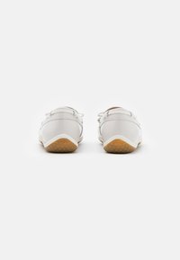 Zapatos de cuero blanco con partes traseras redondeadas, cierres de cordones delgados y suelas de goma con un diseño texturizado para ofrecer agarre y soporte.