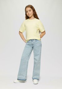 Helles gelbes Kurzarm-T-Shirt, lockere Passform. Hellblaue weit geschnittene Jeans mit fransigem Saum. Weiße Sneakers. Lässiges, entspanntes Outfit.