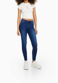 Jeans ajustados de mezclilla azul oscuro con una textura suave, combinados con una camiseta corta blanca con un diseño floral en rosa.