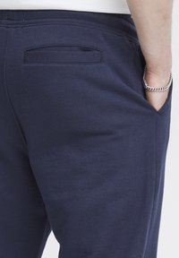 Námornícky modré tepláky s hladkou textúrou, elastickým pásom a jedným zadným vreckom s otváraním na pätku pre pohodlie.
