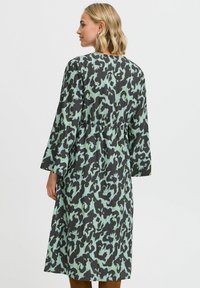 Rochie lungă neagră cu imprimeu abstract de leopard verde, având o croială relaxată, mâneci până la trei sferturi și talie strânsă.