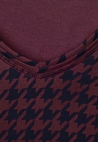Bordově vzorovaný top s designem houndstooth v tmavě námořnické barvě. Hladká textilie s kulatým výstřihem a kontrastním šitím.