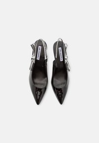 Paar zwarte lakleren slingback-hakken met spitse neus, strikjes en witte bandjes bedrukt met de tekst ""Karl Lagerfeld"", van bovenaf gezien.