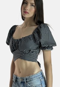 Schwarz-weißer karierter Cropped-Top mit Puffärmeln, gerafftem Vorderteil und Bindeband im Rücken; kombiniert mit hellblauen Jeansshorts.