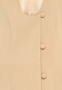 Beige dress with a deep V-neck, featuring smooth fabric, a fitted silhouette, and three circular buttons along the front.