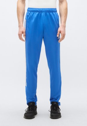 Niebieskie spodnie sportowe z elastycznym paskiem w talii, z białymi paskami po bokach i kieszeniami. Wykonane z gładkiego, lekkiego materiału.