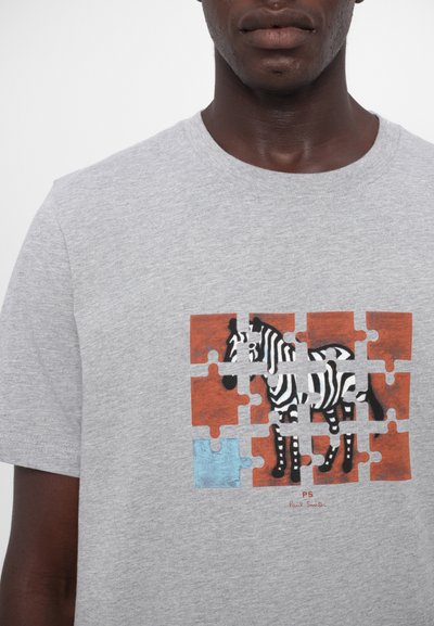 Pilka medvilnės marškinėliai su zebra grafika, įkomponuota dėlionės dizaino, akcentuota raudonomis ir mėlynomis dėlionės detalių kontūrais.