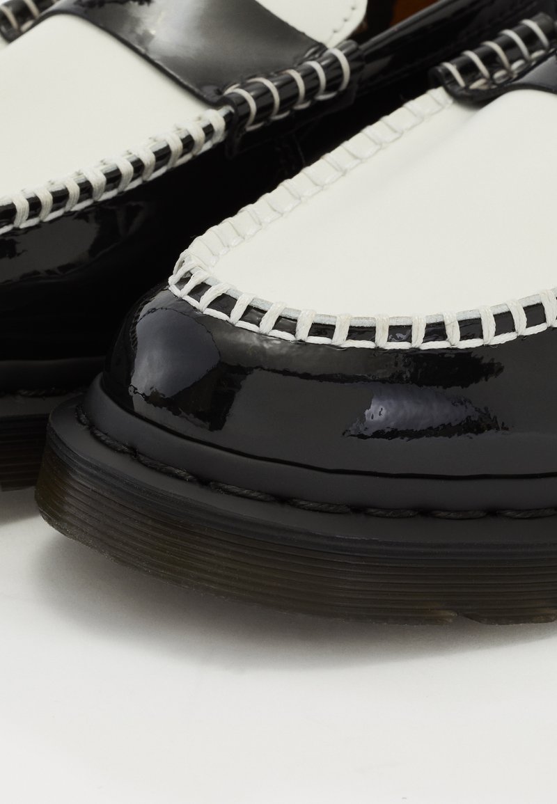 Gros plan de mocassins en cuir noir et blanc avec des semelles épaisses noires et des coutures blanches visibles le long des bords.
