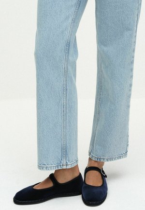 Person iført lyseblå jeans med lige ben og mørkeblå Mary Jane-stil sko med spænde.
