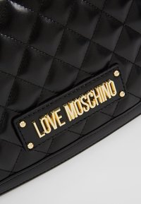 Svart kviltad läderväska med detalj av guldplåt med texten "LOVE MOSCHINO" som är fäst med fyra guldstift.