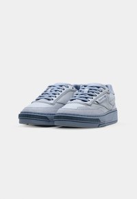 Sneaker blu chiaro con una combinazione di pelle e suede. Presenta dettagli perforati, lacci piatti e una suola spessa e strutturata.