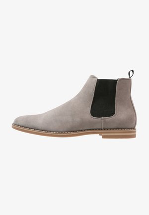 Botte Chelsea en daim gris avec un panneau latéral élastique noir, une semelle beige et une languette à l'arrière, sur fond blanc.