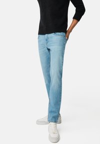 Jasnoniebieskie dżinsy z prostą nogawką, z kontrastowym szwem i subtelną strukturą prania, w połączeniu z białymi trampkami.