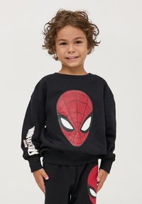 Felpa nera con una grande grafica della maschera di Spider-Man rossa sul davanti, con dettagli in scrittura sulla manica. Tessuto morbido, vestibilità casual.