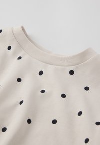 Beige T-shirt met een ronde halslijn, gekenmerkt door marineblauwe stippen in een uniform patroon. Gemaakt van een gestructureerde katoenstof.