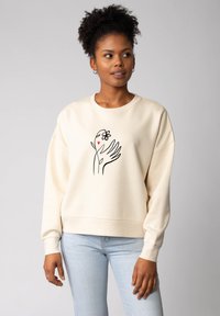 Crème sweatshirt gemaakt van zachte stof, met een zwarte lijntekening van een hand met een bloem en een hart op de voorkant. Ontwerp met een relaxte pasvorm.