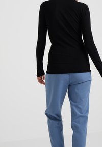 Haut noir à manches longues avec une coupe ajustée, associé à un pantalon ample bleu clair. Texture lisse, détails minimaux et lignes épurées.