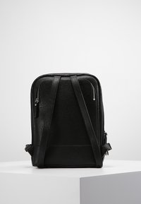 Czarny skórzany plecak o fakturowanym wykończeniu, wydłużonym kształcie, regulowanych paskach na ramiona oraz dwóch kieszeniach na suwak.