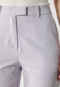 Ljuslila byxor i mjukt tyg med flat front, bälteshällor och en subtil lyster, utan synliga mönster eller detaljer.