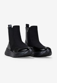 Bottines noires avec panneaux latéraux élastiques, dessus texturé, accents en cuir verni lisse et semelle extérieure en caoutchouc moulé. Fermeture éclair sur un côté.