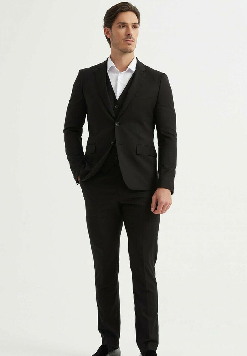 Costume noir sur mesure avec une veste à simple boutonnage, deux poches avant et une chemise blanche en dessous. Un pantalon slim complète le look.
