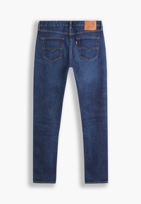 Jean en denim bleu vu de dos avec deux poches cousues, un patch en cuir de la marque à la ceinture et une étiquette rouge sur la poche droite.