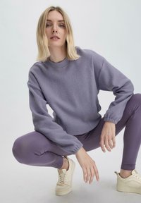 Fliederfarbener Fleece-Sweatshirt mit geripptem Halsausschnitt und Bündchen, kombiniert mit passenden Leggings. Beigefarbene Sneakers mit glatter Oberfläche.