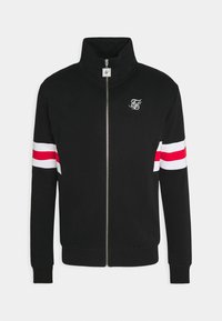 Chaqueta negra con cremallera y alto cuello, con rayas blancas y rojas en las mangas, y un pequeño logo blanco en el lado izquierdo del pecho.