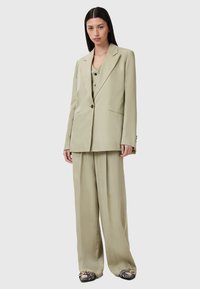 Completo su misura verde chiaro composto da un blazer doppiopetto, pantaloni a gamba larga e dettagli neri sui bottoni. Tessuto morbido e fluido.