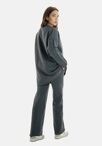 Felpa grigia oversize e pantaloni coordinati realizzati in morbido tessuto, caratterizzati da una vestibilità comoda e orlo arrotondato. Scarpe: sneakers bianche.