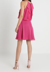 Fuchsia ärmlös klänning med lager av volanger, nyckelhålsryggdetalj, utsvängd nederkant och matchad med ljusrosa ankelremsskor.