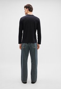 Camisa preta de mangas longas com um decote redondo, combinada com jeans azuis claros de corte solto, apresentando um design clássico de cinco bolsos.