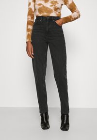 Vysoké černé džíny z denimu s rovnými nohavicemi a pěti kapsami, doplněné černými botami na podpatku.