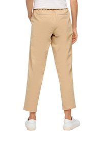 Beige, lichtgewicht broeken met een relaxte pasvorm, elastische tailleband en achterzakken. Gecombineerd met witte sneakers.