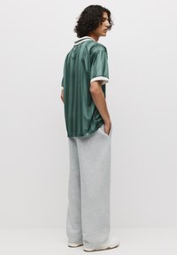 Grøn skjorte med lodrette striber og korte ærmer, med en hvid krave, parret med løstsiddende grå sweatpants og hvide sneakers.