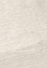 Hellbeige gestrickter Stoff mit einer weichen Textur. Verfügt über einen gerippten Saum und subtile Variationen im Faden für optisches Interesse.