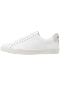 Baskets en cuir blanc avec lacets plats, semelle en caoutchouc texturée et un accent en daim gris doux au talon. Design minimaliste et détail du logo.