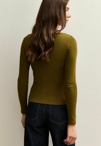 Oliwkowozielony, długi rękaw z dopasowaną prążkowaną fakturą. Noszony z ciemnym, wysokim stanem dżinsu, prezentujący minimalistyczny design.