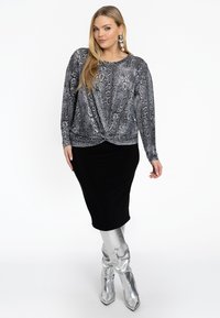 Schwarze knielange Rock kombiniert mit einem langen grauen Oberteil mit Schlangenprint. Glänzende silberne knief hohe Stiefel runden das Outfit ab.