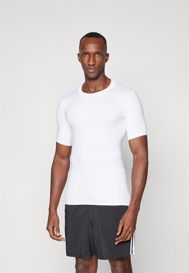 Hvit treningst-skjorte med korte ermer laget av et elastisk og glatt stoff, kombinert med sorte shorts. Enkel rund hals, kroppsnær passform.