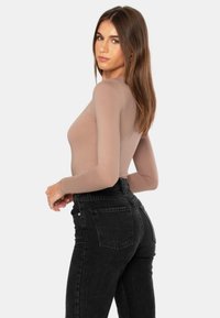 Pitkähiha beige paita, jossa on tiukka muotoilu, yhdistettynä korkeavyötäröisiin mustiin farkkuihin, joissa on klassinen viiden taskun tyyli ja kevyt haalistuma.