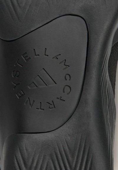 Black athletic shoe sole featuring textured design and embossed logo with three stripes. Smooth materials with distinct patterns and accents.