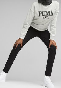 Felpa grigia cropped con logo "PUMA", pantaloni neri aderenti e sneakers bianche. L'outfit presenta un design minimalista e uno stile casual.