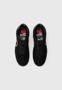 Juodi veliūriniai sportbačiai su apvaliu pirštu, tekstūruota viršūne ir juodais raišteliais. Viduje yra raudona širdies logotipo su tekstu "LOVE MOSCHINO".
