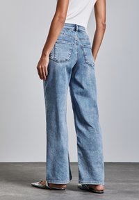 Ljusblå denimbyxor med vida ben, bakfickor och råkant. Har hög midja och subtila blekningar. Kombineras med spetsiga flats.