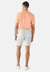 T-shirt in cotone leggero color pesca, abbinato a pantaloni corti a righe blu e bianche con elastico in vita e tasche posteriori. Sneakers bianche.