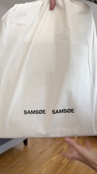 Baltos medvilnės maišelis su raišteliu, apačioje su dviem juodais "SAMsøE" logotipais. Lygus paviršius, šiek tiek susiraukšlėjęs, ir surištas viršus.